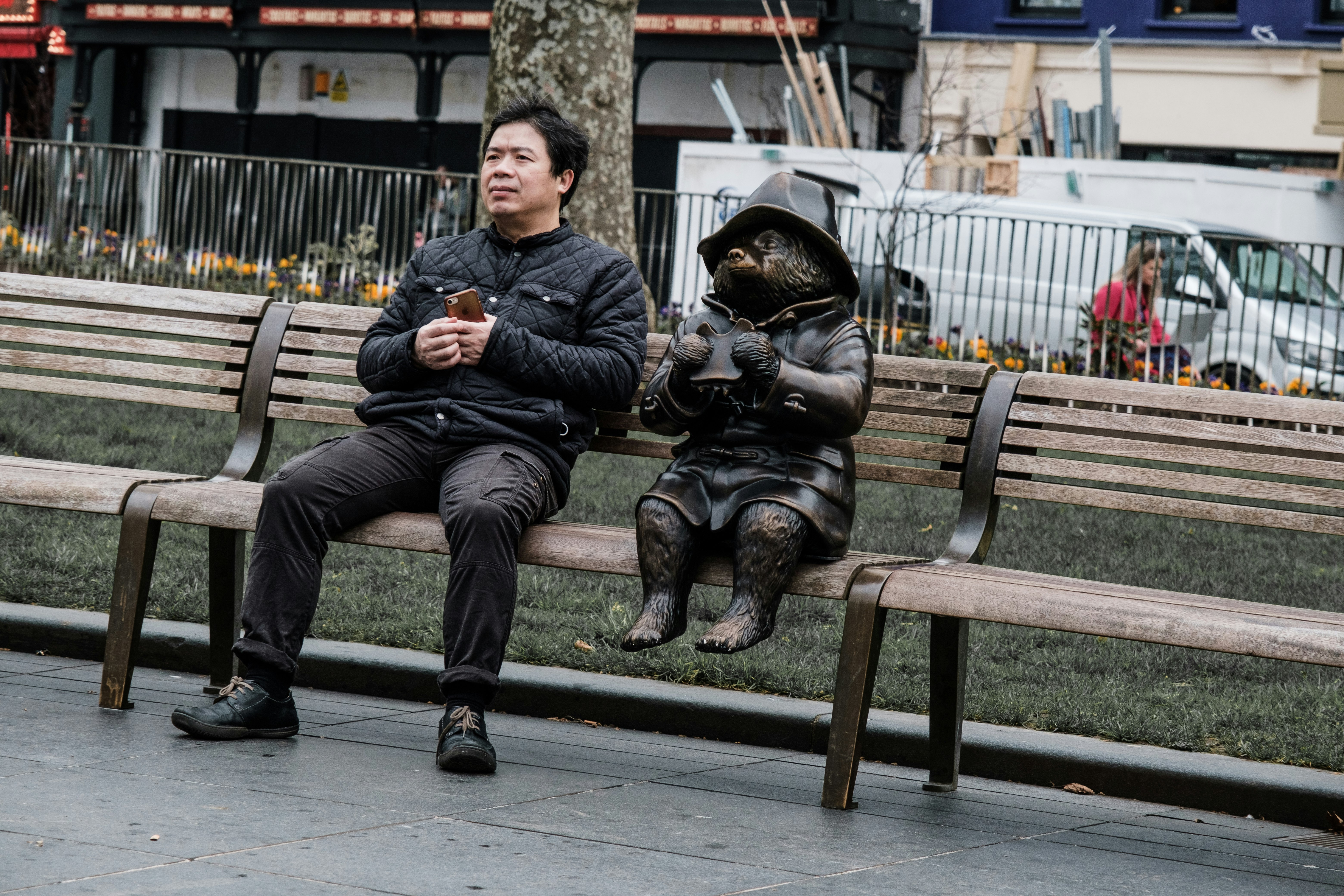 man in black jacket sitting on brown wooden bench